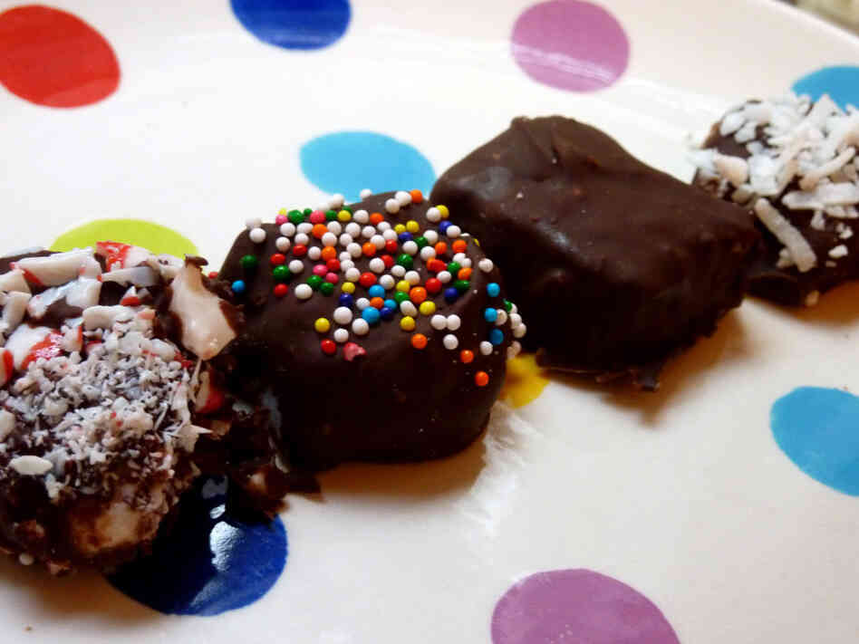 Marshmallows dipped in chocolate and various sprinkles sit on a polka-dot plate