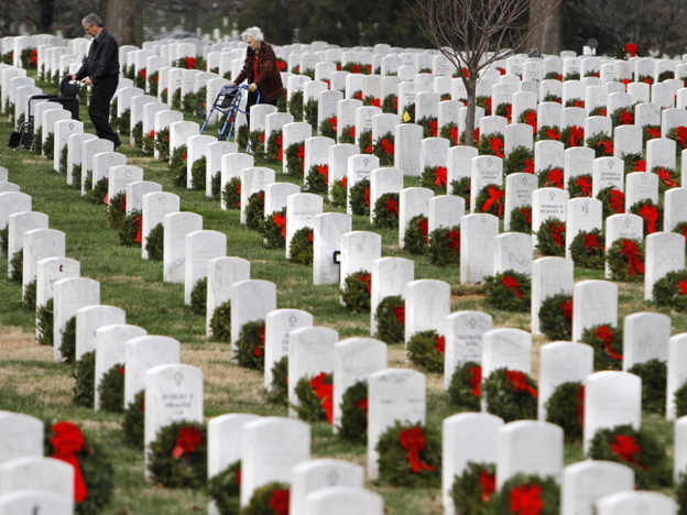 Visitors walk among gravestones adorned with seasonal Christmas wreaths at Arlington National Cemetery.