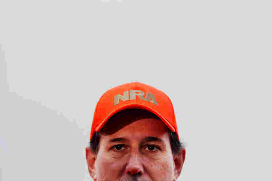 Former Sen. Rick Santorum dons a National Rifle Association hat while talking to reporters at Doc's Hunt Club in Adel, Iowa, on Dec. 26. 