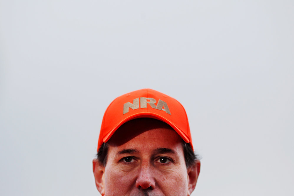 Former Sen. Rick Santorum dons a National Rifle Association hat while talking to reporters at Doc's Hunt Club in Adel, Iowa, on Dec. 26. 