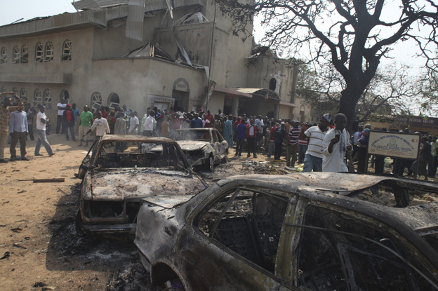 Onlookers gather around a destroyed car at a Catholic church bombed on Christmas Day. A violent Islamist group claimed responsibility for the deadly attack. 