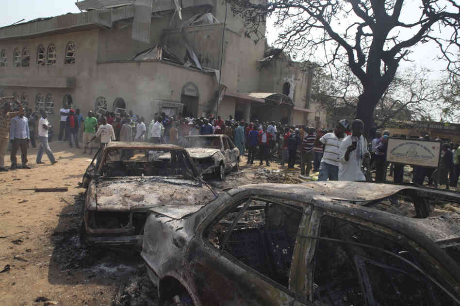 Onlookers gather around a destroyed car at a Catholic church bombed on Christmas Day. A violent Islamist group claimed responsibility for the deadly attack. 