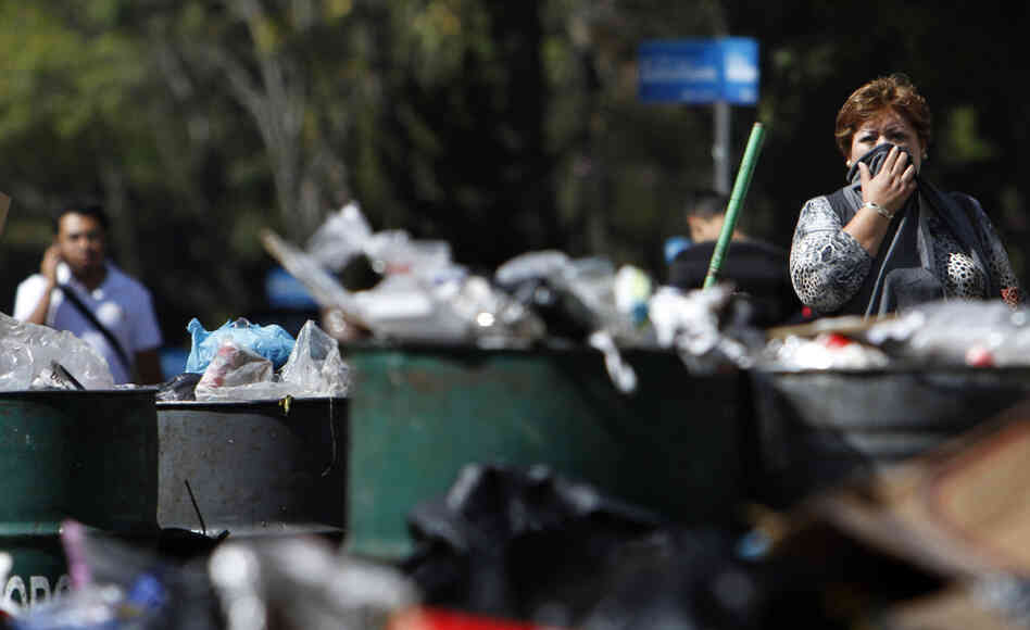 A woman covers her face as she walks past piled up garbage in downtown Mexico City. A woman covers her face as she walks past piled up garbage in downtown Mexico City.