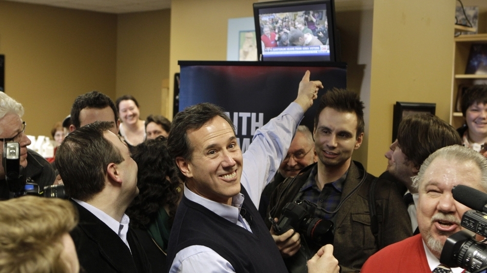 Republican presidential candidate Rick Santorum points to a television showing his campaign stop on live at the Daily Grind coffee shop in Sioux City, Iowa, Sunday.