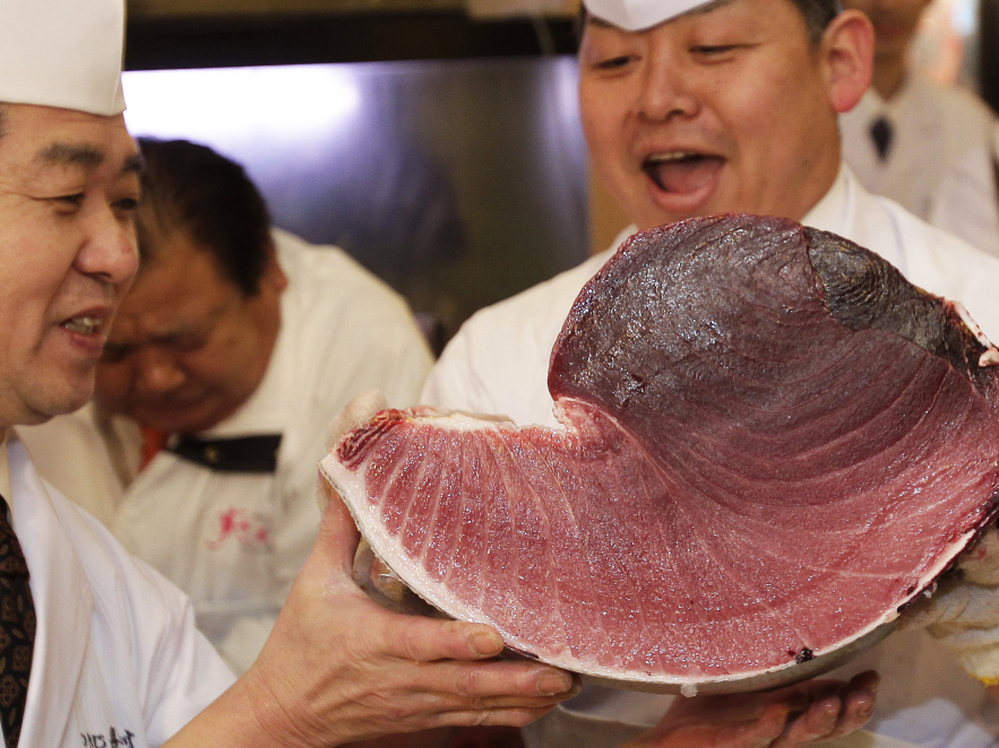 Sushi chefs of Kiyomura Co. hold a slice of a bluefin tuna near the Tsukiji fish market in Tokyo. The bluefin tuna caught off northeastern Japan fetched about $736,000 Thursday in the first auction of the year at the fish market.