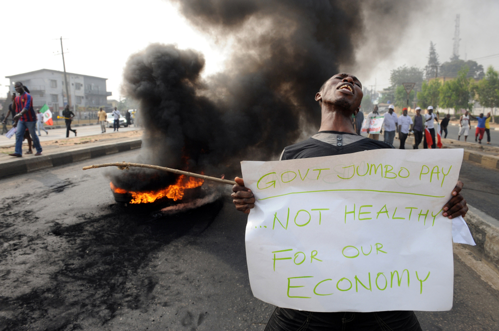 A man carries a placard beside a bonfire during Monday's demonstration against soaring petrol prices following government's decision to abolish decades-old fuel subsidies.