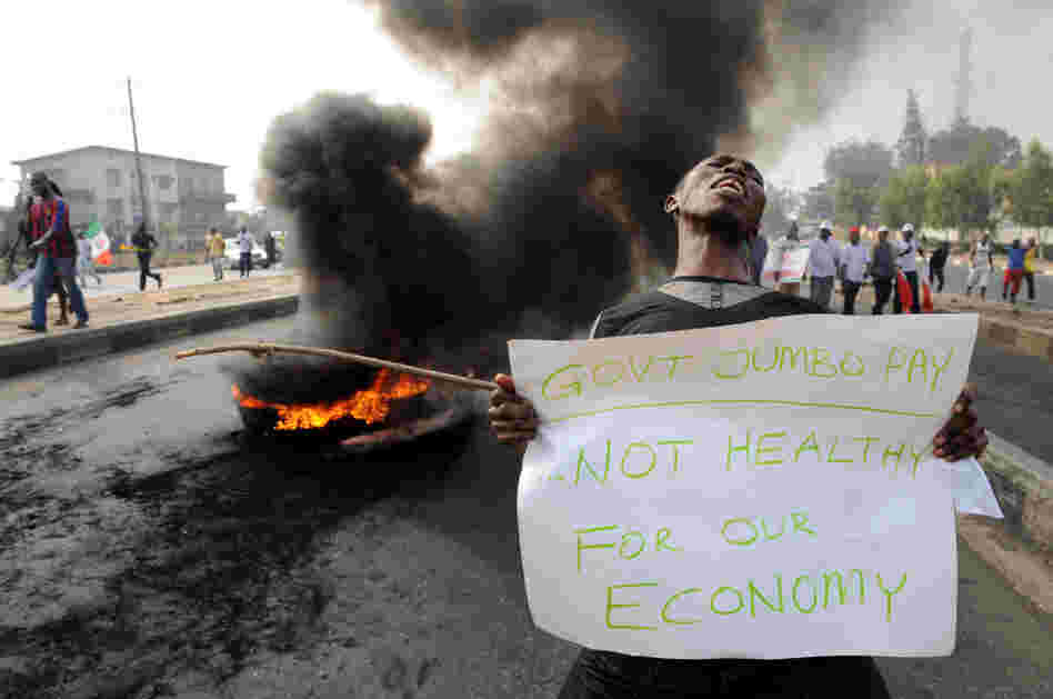 A man carries a placard beside a bonfire during Monday's demonstration against soaring petrol prices following government's decision to abolish decades-old fuel subsidies.