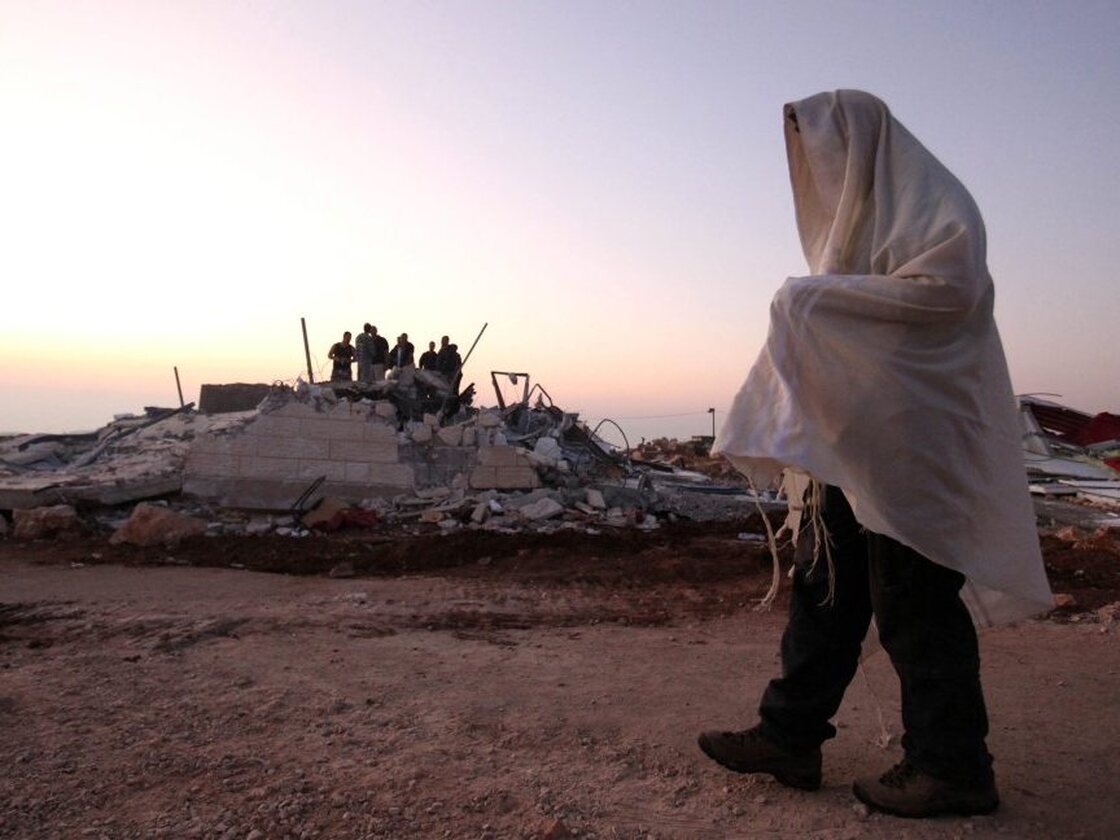A Jewish settler wears his prayer shawl as he passes one of the structures demolished at the unauthorized Jewish settlement outpost in Ramat Migron, in the West Bank, on Sept. 5, 2011. Israel's radical Hilltop Youth have built numerous such outposts in recent years. 