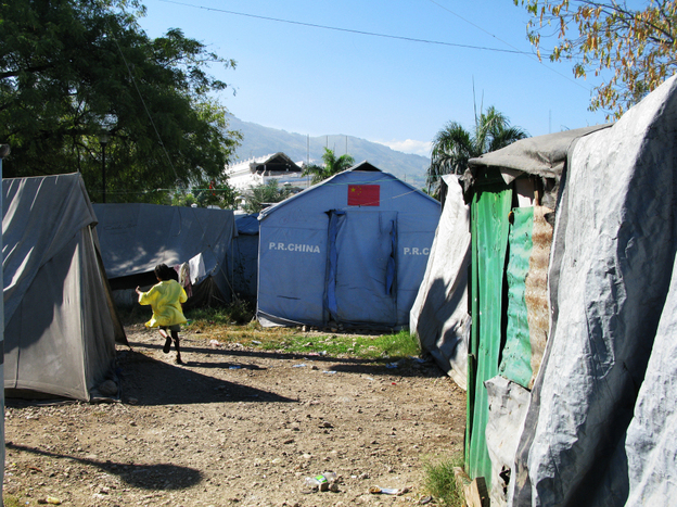At the Place Pigeon camp, residents bathe in the streets by pouring water over themselves from a basin. 