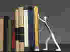 A bookend shaped like a person, holding up a row of books