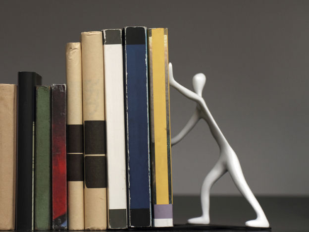 A bookend shaped like a person, holding up a row of books