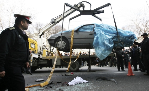 People gather around a car as it is removed by a mobile crane in Tehran, Iran. The car was being driven by Iranian nuclear scientist Mostafa Ahmadi Roshan when it was targeted by a bomb Wednesday. Roshan was killed in the blast.