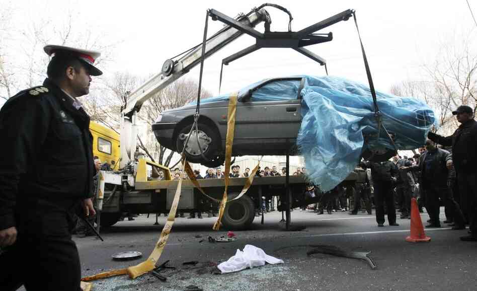 People gather around a car as it is removed by a mobile crane in Tehran, Iran. The car was being driven by Iranian nuclear scientist Mostafa Ahmadi Roshan when it was targeted by a bomb Wednesday. Roshan was killed in the blast.