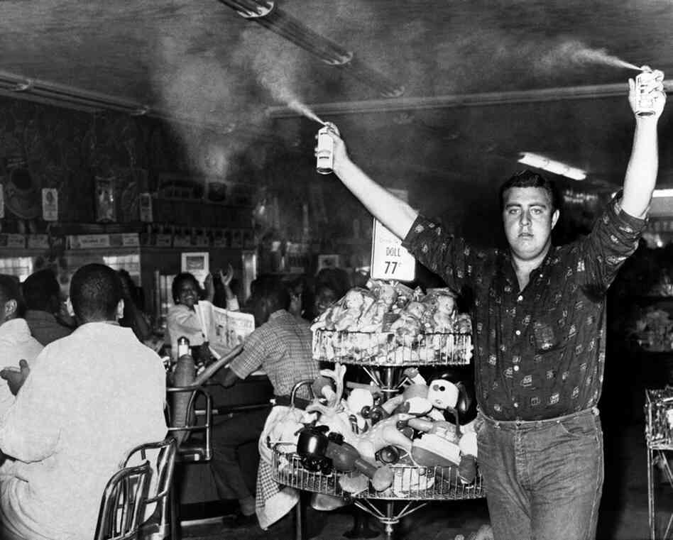 A white youth sprays insect repellent above the heads of nearly 100 African-Americans demonstrating at a lunch counter in Atlanta.  