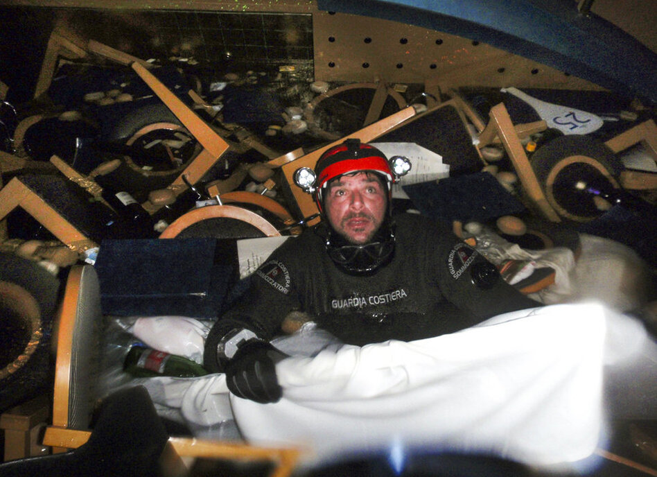 A scuba diver makes his way through floating pieces of furniture while searching for people inside the cruise ship.