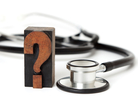A question mark on a wood block stands next to a stethoscope. A question mark on a wood block stands next to a stethoscope.