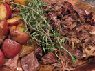 A copper platter holds braised goat meat and potatoes, garnished with rosemary A copper platter holds braised goat meat and potatoes, garnished with rosemary