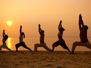 Five people on a beach stand in the warrior pose.