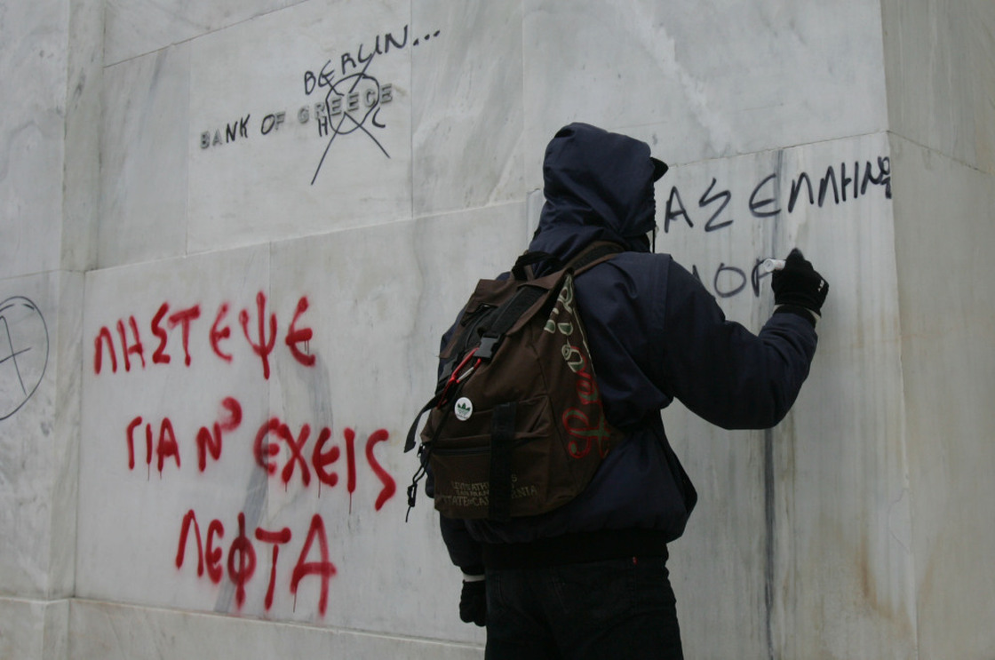 Protesters write on the wall of the National Bank of Greece during a demonstration involving thousands in Athens on Friday.
