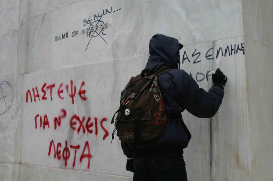 Protesters write on the wall of the National Bank of Greece during a demonstration involving thousands in Athens on Friday.
