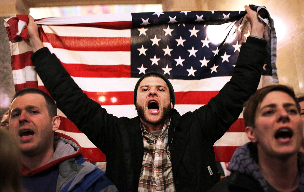 For so many reasons, Americans are seething. Here, a protester shouts as he holds an American flag after storming the Wisconsin state Capitol in Madison last March, after Republicans in the state Senate voted to curb collective bargaining rights for public workers.