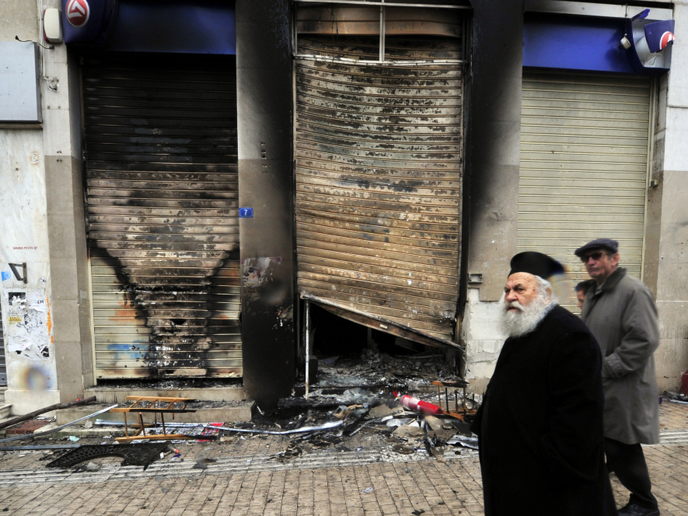 A Greek priest walks past a burned branch of the Eurobank in central Athens on February 13.