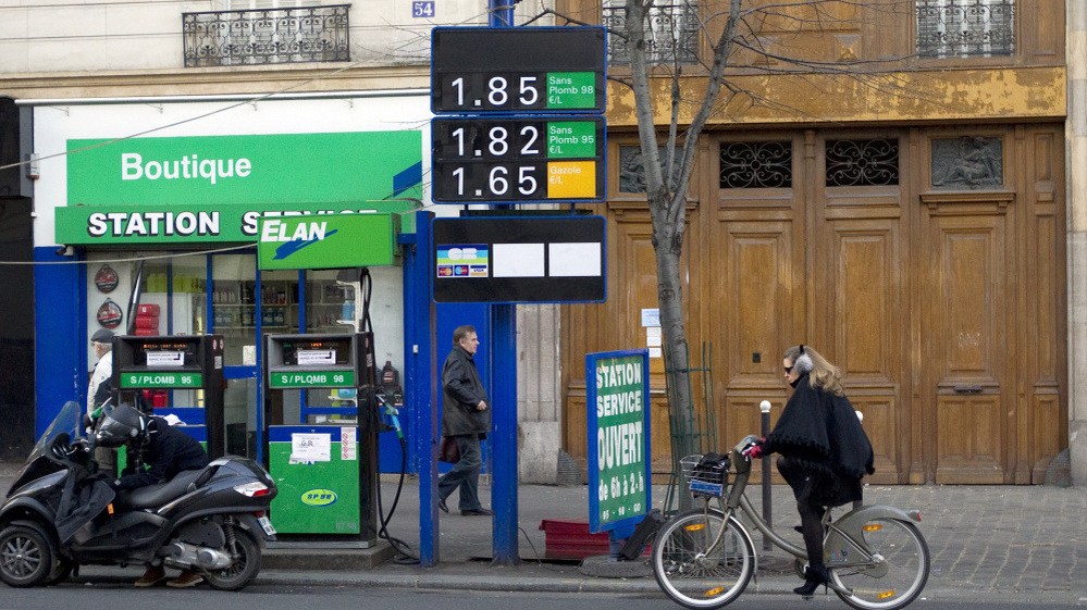 Gas prices in France have topped more than $8 a gallon in some areas. In this photo from January, a woman rides her bike past a gas station in Paris.