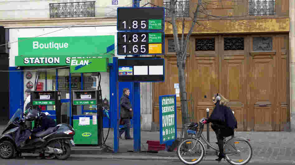 Gas prices in France have topped more than $8 a gallon in some areas. In this photo from January, a woman rides her bike past a gas station in Paris.