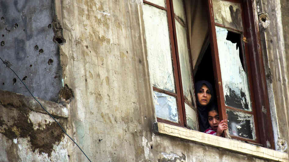 The fighting in Syria was seen as a spark for clashes in the Lebanese city of Tripoli last week. Here a Lebanese woman and her daughter look out the window of their bullet-pocked home in Tripoli on Sunday, Feb. 12.  