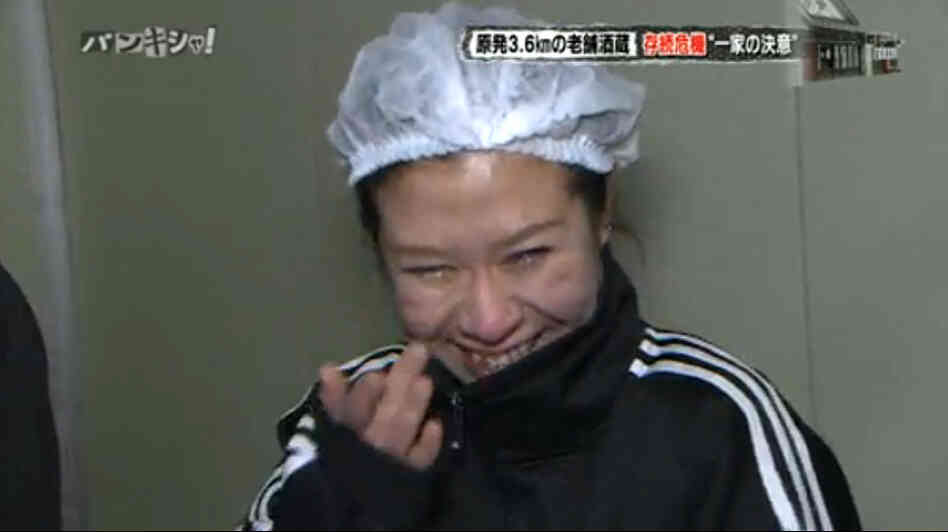 A woman wipes tears from her eyes as she smiles after tasting the sake she and her father made — their first batch since the Fukushima disaster forced them to leave their ancestral brewery. 