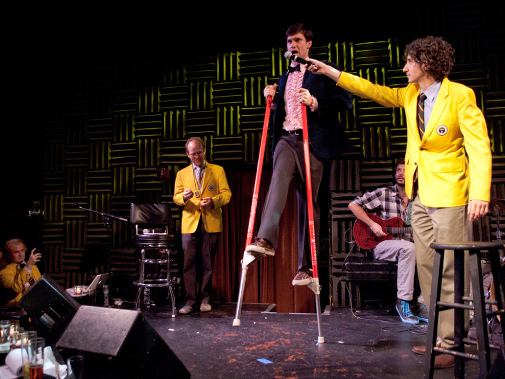 Dan Rollman, the co-founder of RecordSetter, holds up a microphone to Rob Lathan, who currently holds the world record for completing 81 leg kicks on stilts while singing "New York, New York," at a World Record Appreciation Society event in New York City. 