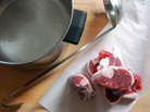 A large pot and ladle sit on a counter next to a pile of beef shanks on butcher paper. A large pot and ladle sit on a counter next to a pile of beef shanks on butcher paper.