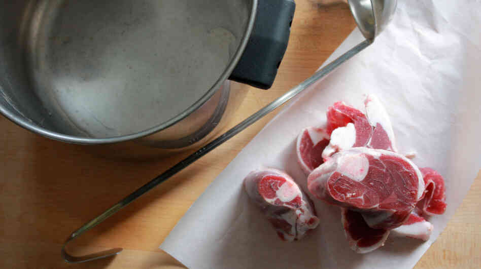 A large pot and ladle sit on a counter next to a pile of beef shanks on butcher paper.