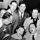Bert Lahr (far right), Ray Bolger (back row, right), Judy Garland (sitting, right), composer Harold Arlen (sitting left), and various MGM and music publishing executives sing songs from the 1939 film musical 'The Wizard of Oz' around a microphone in the NBC radio studio, circa 1939. 