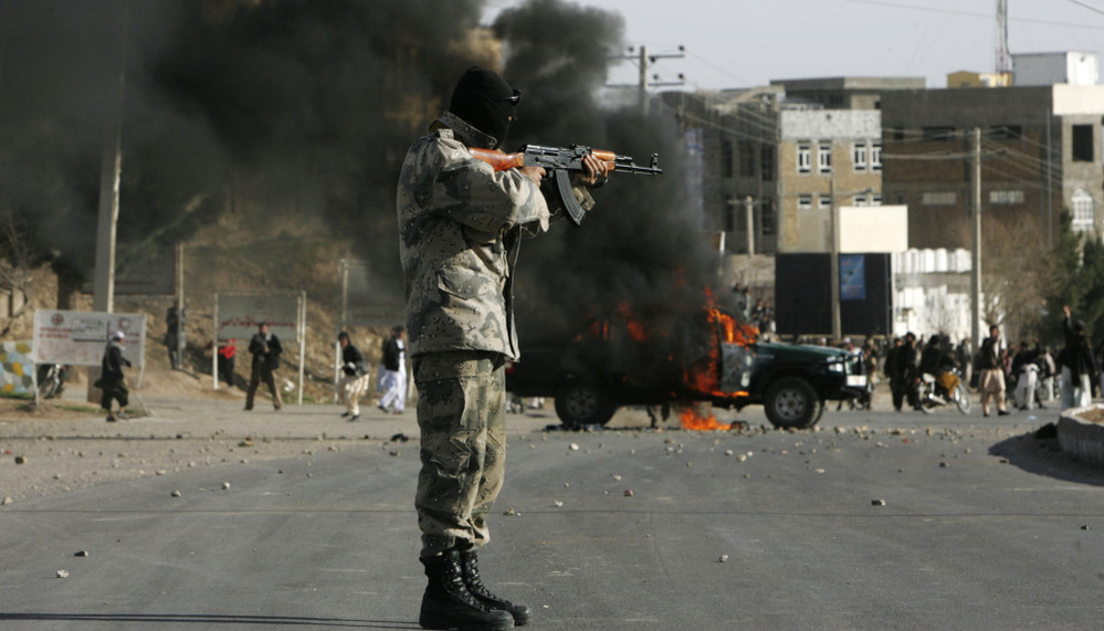 An Afghan policeman aims at protesters by a burning police truck set alight during an anti-U.S. demonstration on Friday over burning of Qurans at a U.S. military base in Afghanistan.