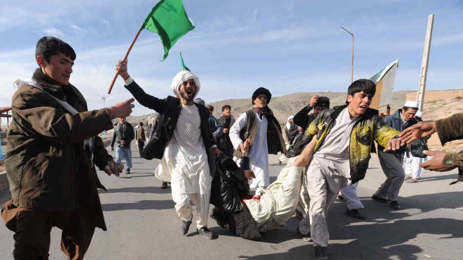 The latest violence in Afghan has raised doubts about the U.S. strategy. Here, Afghan demonstrators shout anti-U.S. slogans as they carry a wounded man during a protest in the Western city of Herat on Feb. 24.
