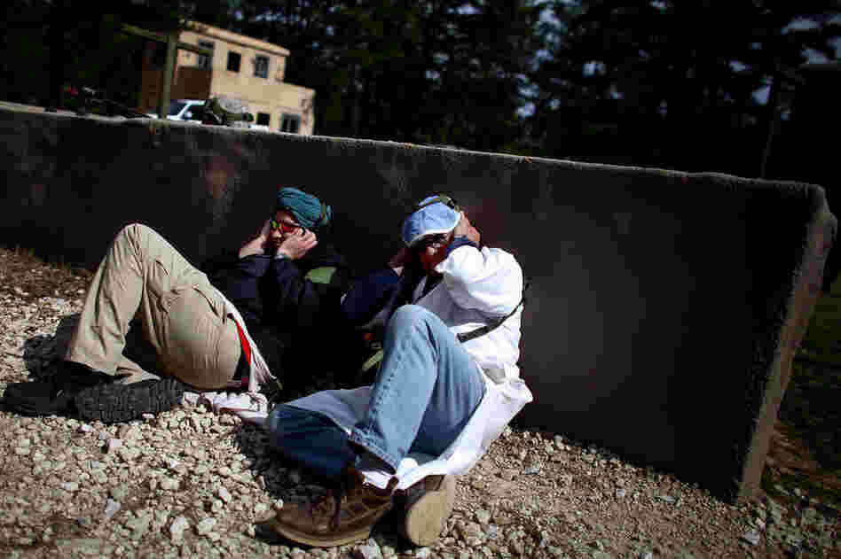 Afghan role-players cover their ears and hide behind a wall during a gun battle.