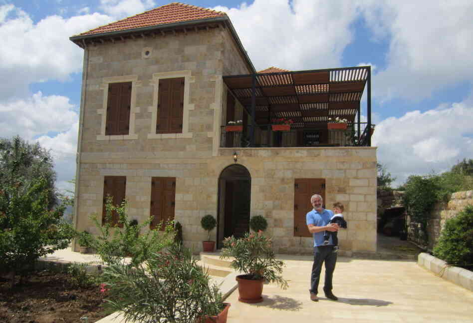 Shadid holds his son in front of the family home he spent years renovating in Marjayoun, Lebanon.