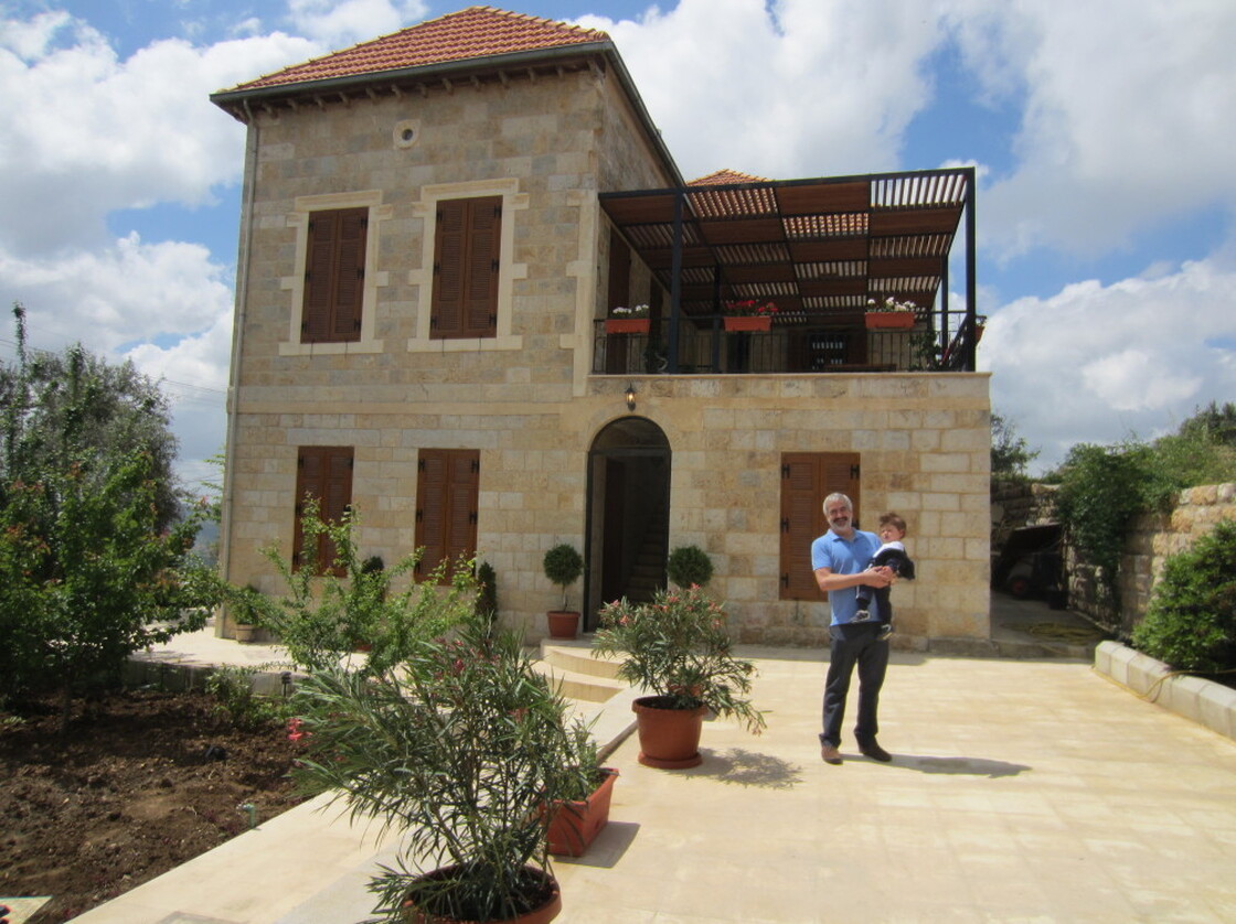 Shadid holds his son in front of the family home he spent years renovating in Marjayoun, Lebanon.