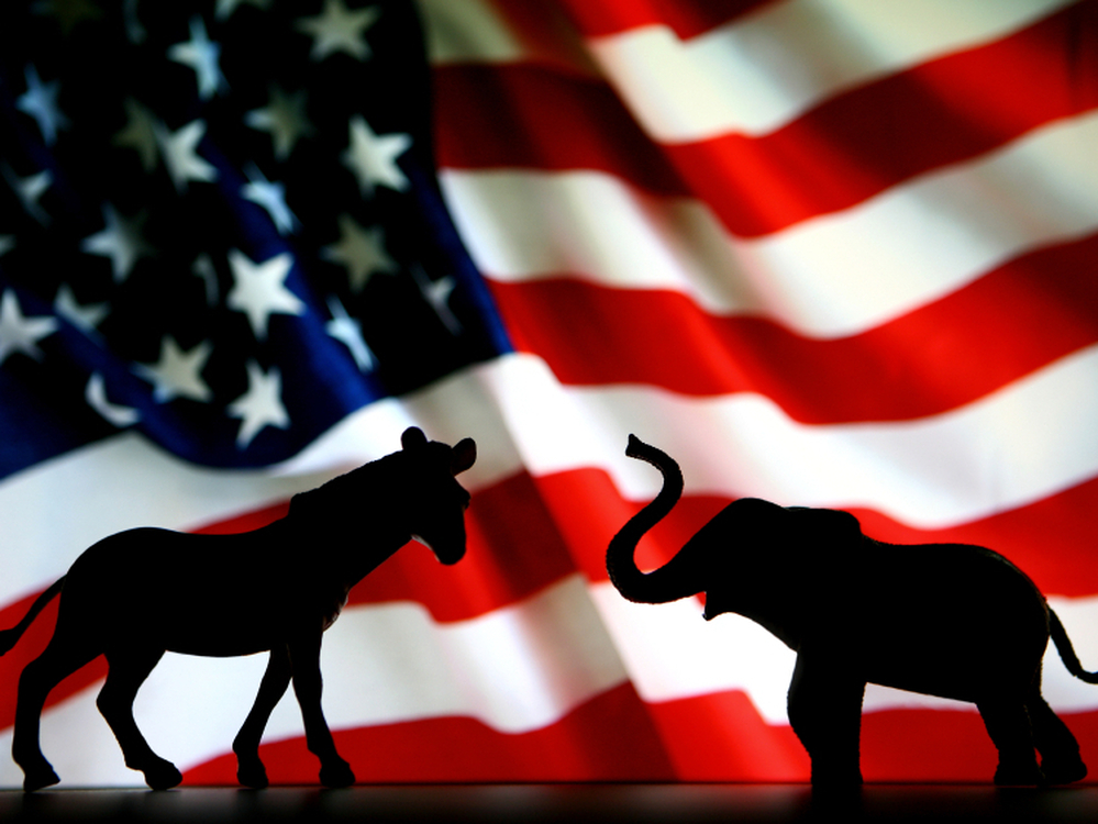 The symbols of the two political parties, the donkey for the Democrats and the elephant for the Republicans, battle it out in front of the American flag. 