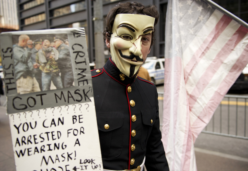 A young man with wearing a military uniform and mask usually associated with the group anonymous marches with Occupy Wall Street protesters in this November.