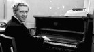 Jerry Lee Lewis smiles over his shoulder while playing the piano in a dressing room. Jerry Lee Lewis smiles over his shoulder while playing the piano in a dressing room.