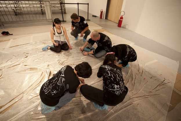 Before the explosion, volunteers help prepare the enormous canvases with cardboard stencils.