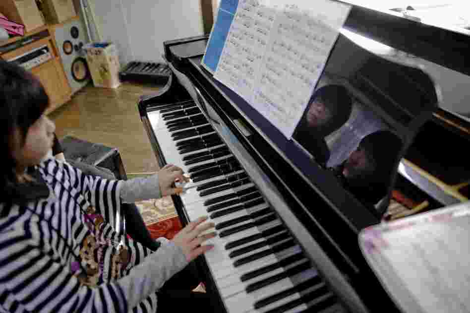 Piano teacher Manami Kuga, seen reflected on the left, instructs Kyoka. Two of Kuga's students, Hana and Kento Suzuki, died during the tsunami. Kento's body was found three weeks after the storm; Hana's body is still missing.