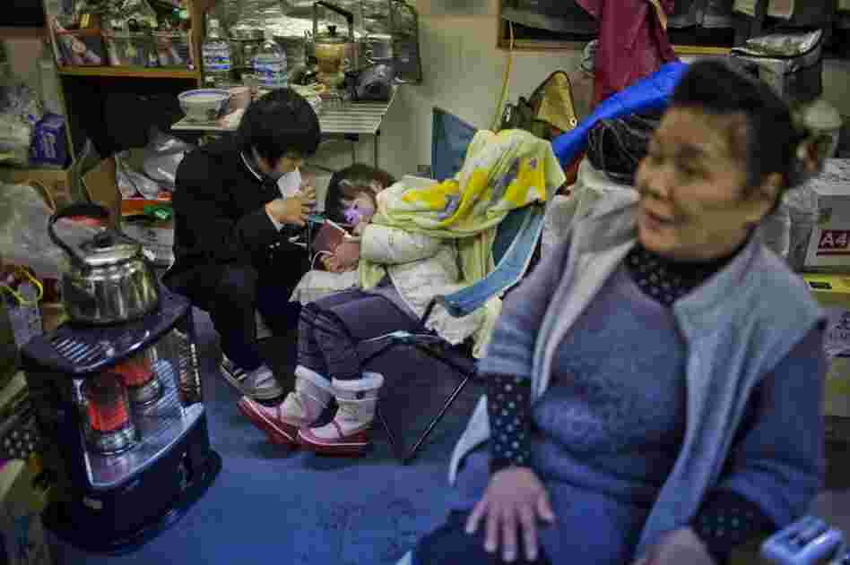 Kikuko Abe, 65, looks on as her grandchildren, Iroha Kodama, 8, and Naiki Kodama, 15, play hand-held video games in a temporary community center.