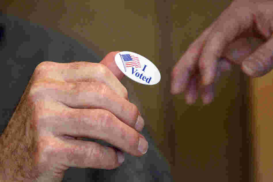 Madison United Methodist Church precinct worker Bob Shirley hands a "I Voted" sticker to a voter in Madison, Miss. 