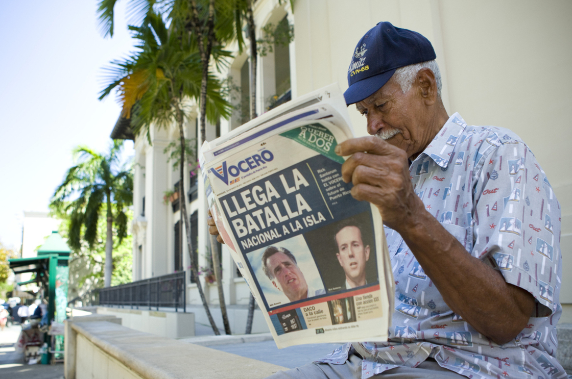Carlos Diaz, 84, reads local newspaper "El Vocero" with a front page depicting both Mitt Romney and Rick Santorum and a headline reading, "The National Battle Arrives on the Island." 