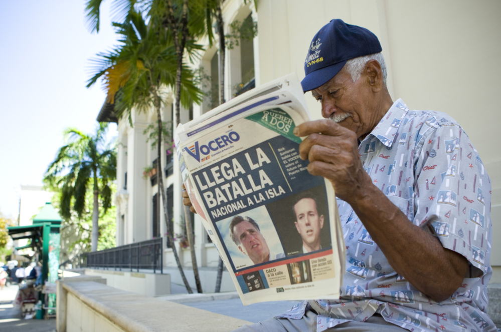 Carlos Diaz, 84, reads local newspaper "El Vocero" with a front page depicting both Mitt Romney and Rick Santorum and a headline reading, "The National Battle Arrives on the Island." 
