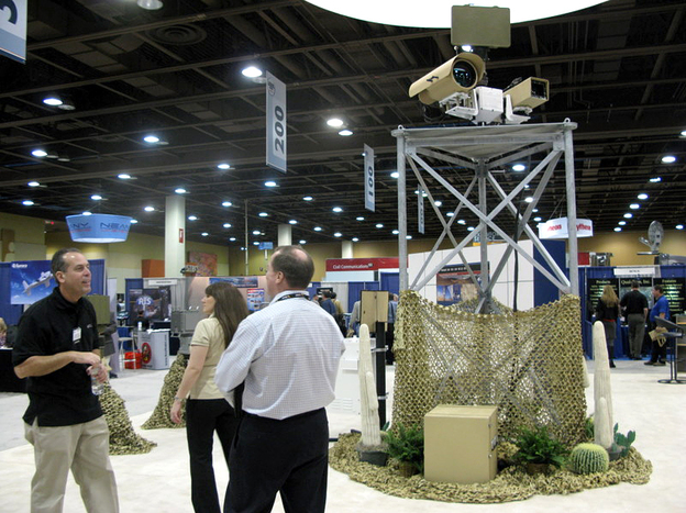 A vendor talks to attendees at the  Border Security Expo in Phoenix, Ariz., next to a display of sophisticated cameras and sensors painted to blend into the desert.