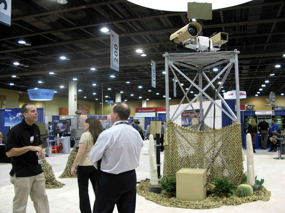 A vendor talks to attendees at the  Border Security Expo in Phoenix, Ariz., next to a display of sophisticated cameras and sensors painted to blend into the desert.